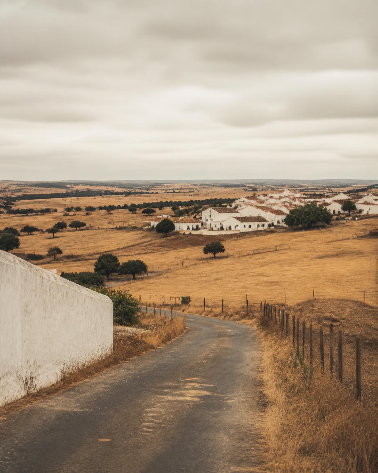 Estrada rural a descer para uma aldeia branca no Alentejo interior