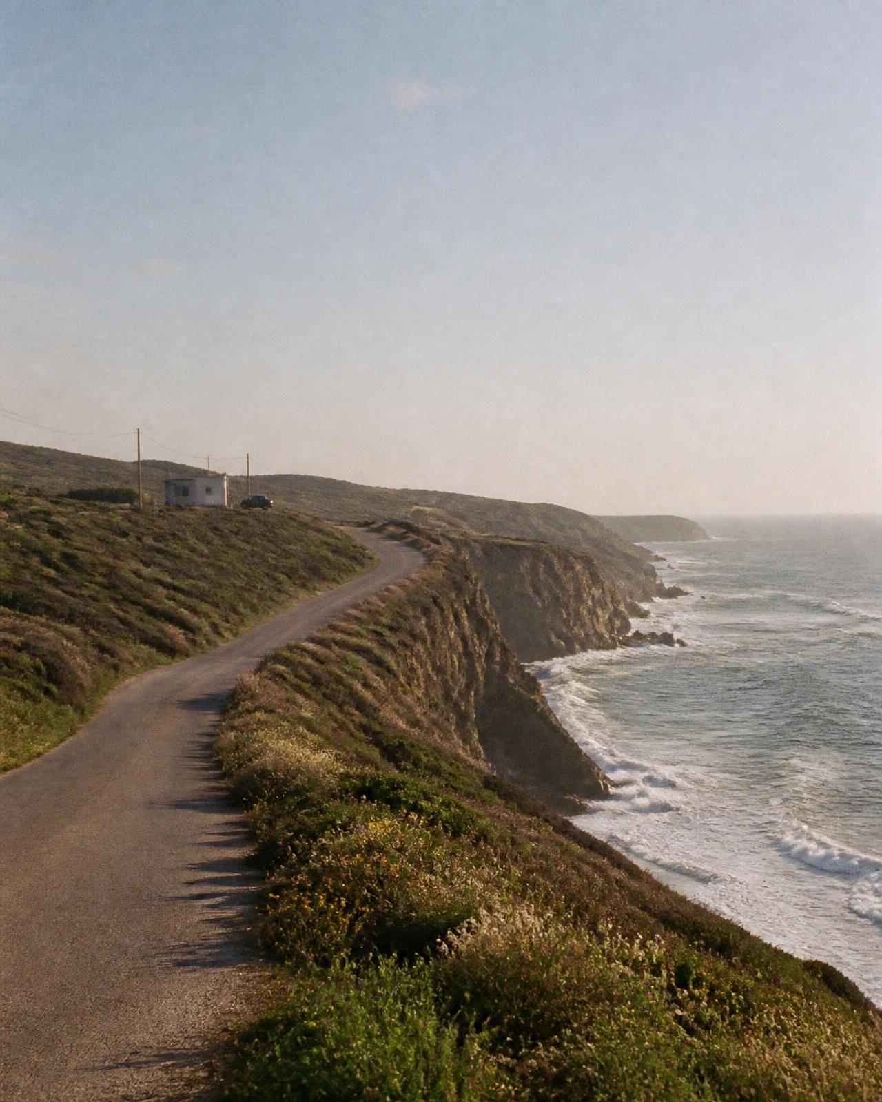 Estrada estreita ao longo das falésias da Costa Vicentina, com o Atlântico ao fim da tarde